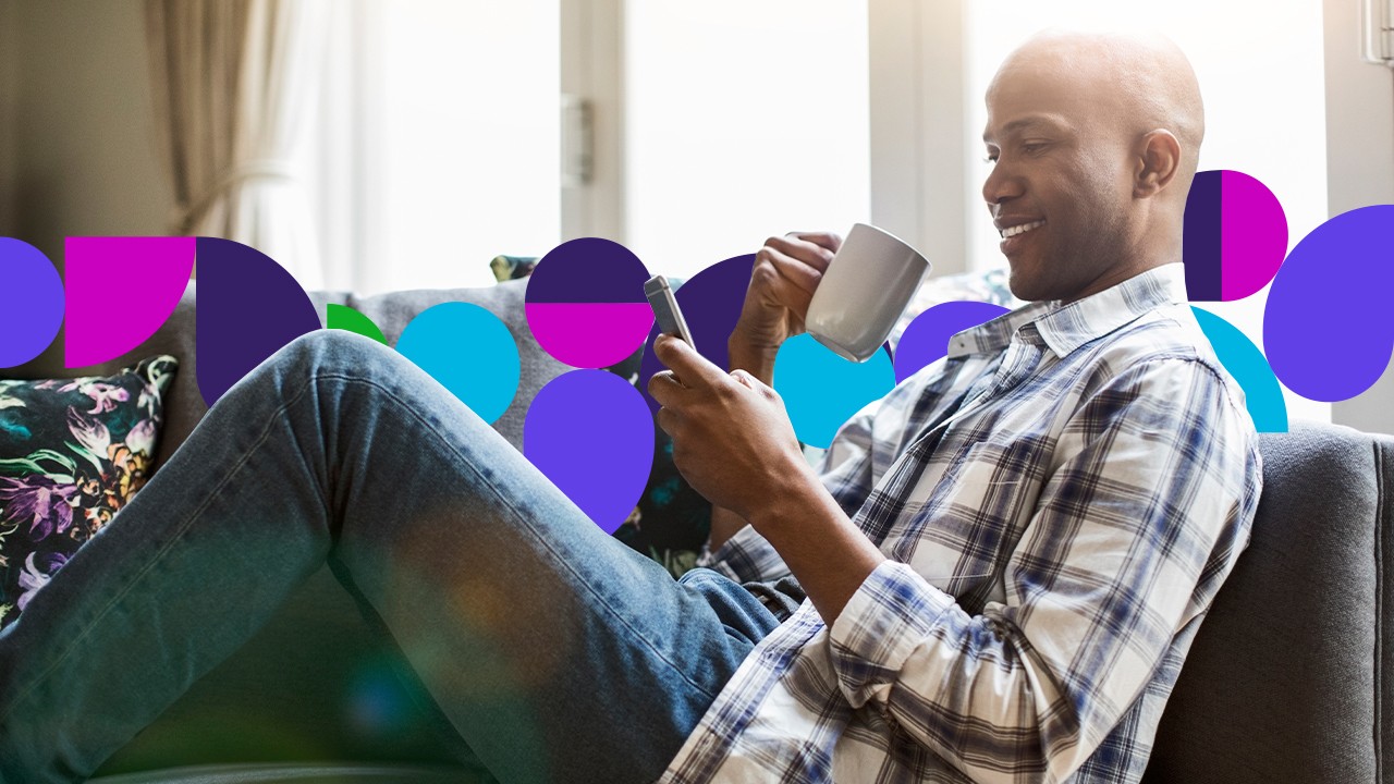 Man sitting on couch looking at tablet holding a coffe cup