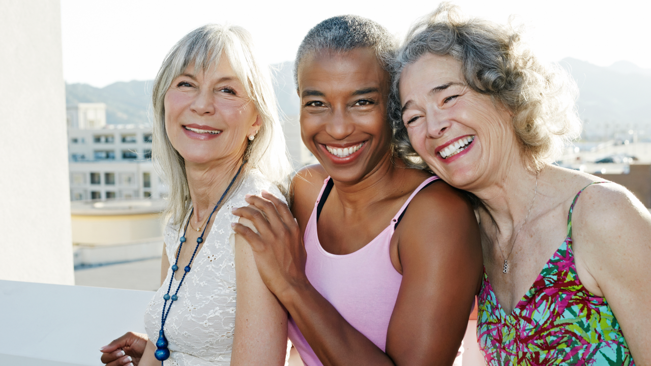 Three smiling women standing together with city buildings in the background