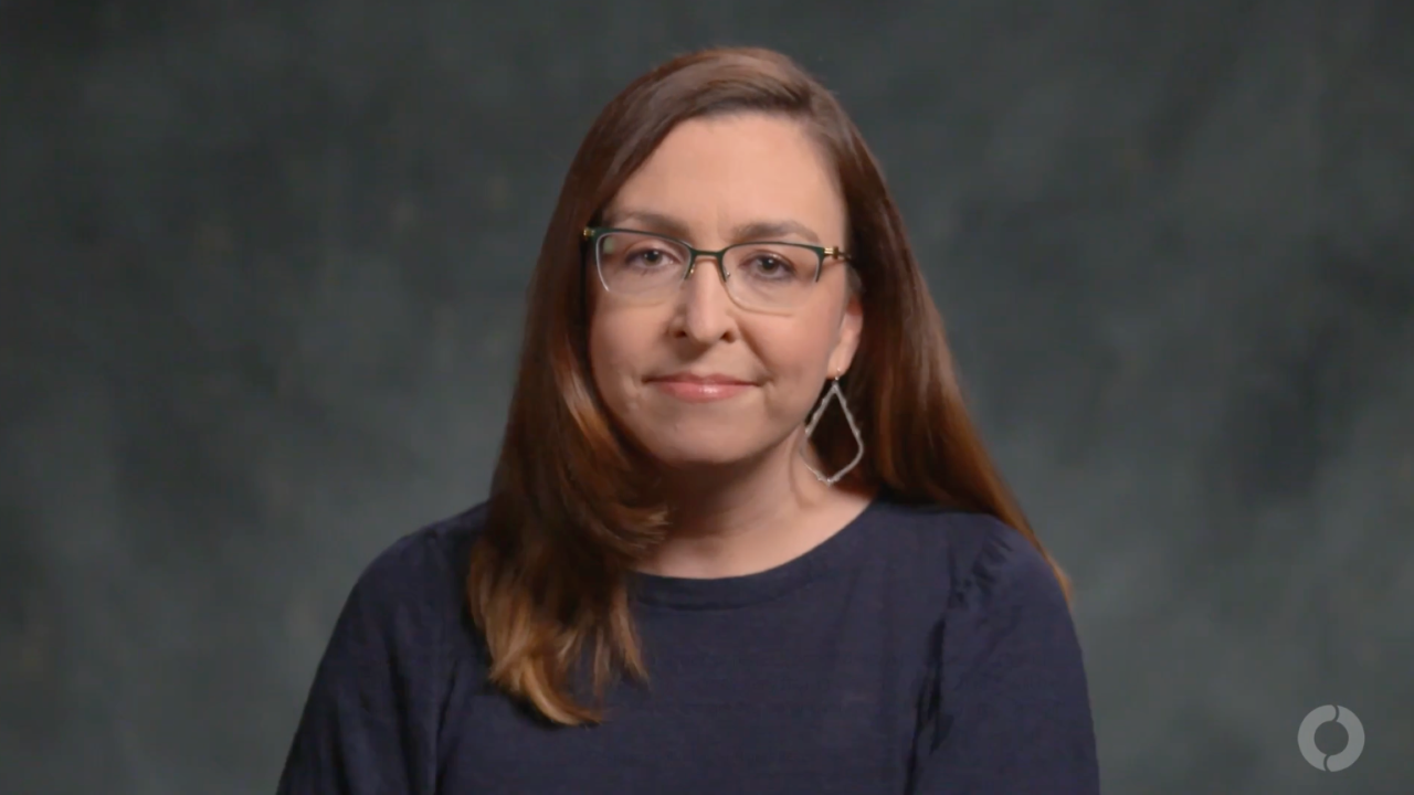 Portrait of a woman with glasses looking at the camera against a dark background.