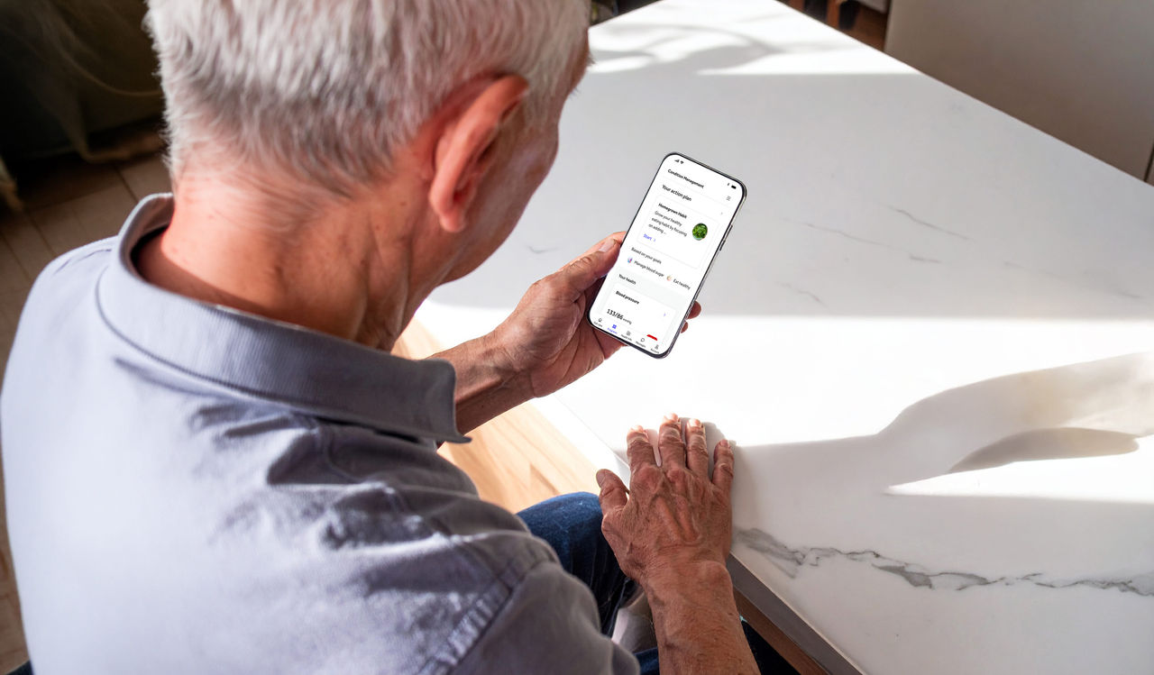 Senior man sitting at a counter looking down at his mobile phone