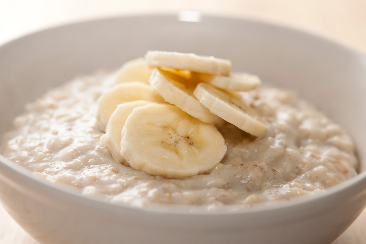A bowl of creamy oatmeal topped with fresh banana slices, placed on a wooden surface, with a soft, warm light illuminating the dish.