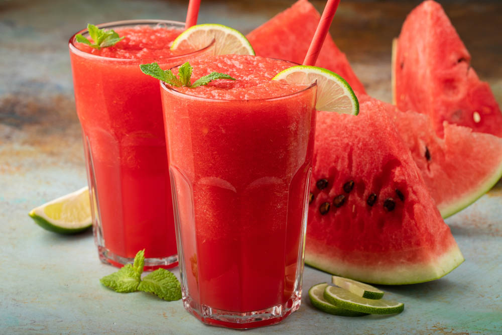 Watermelon slushie with lime, summer refreshing drink in tall glasses on a blue rusty background.