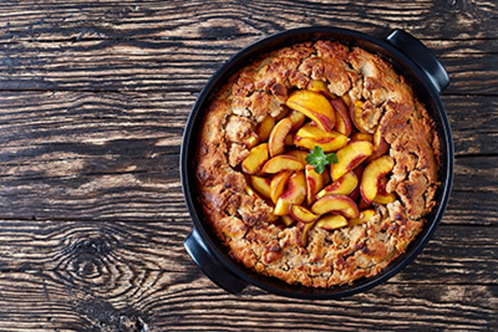 Homemade Peach Cobbler with crisp topping in a black dish, made from fresh summer peaches, horizontal view from above, flat lay