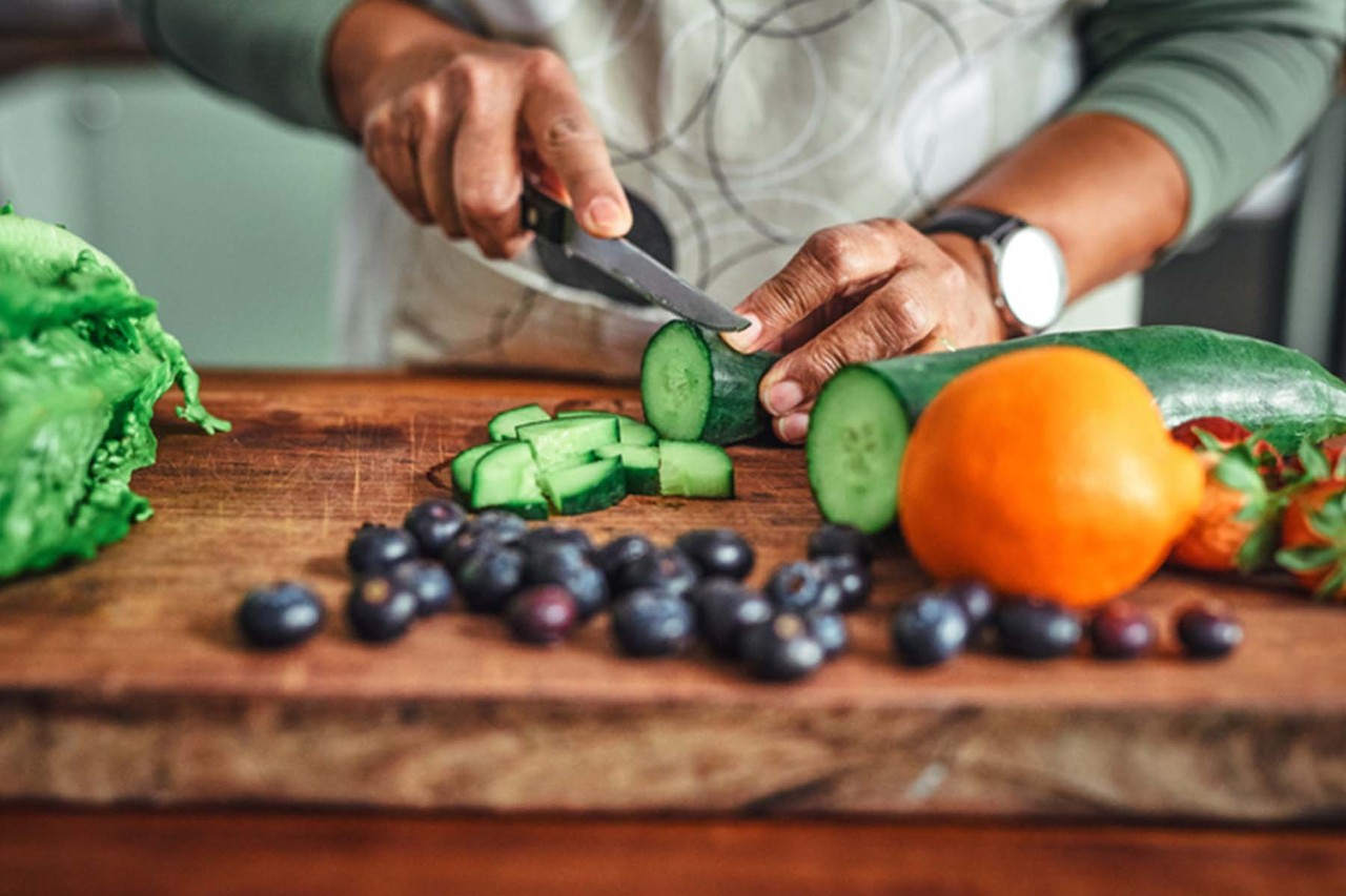 A close-up image of a person slicing cucumber on a wooden cutting board.