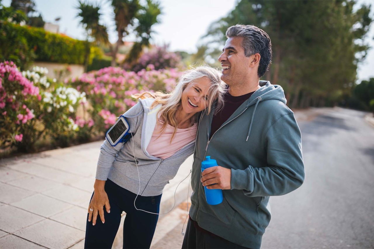 Man and woman in athletic clothing smiling while walking outdoors.