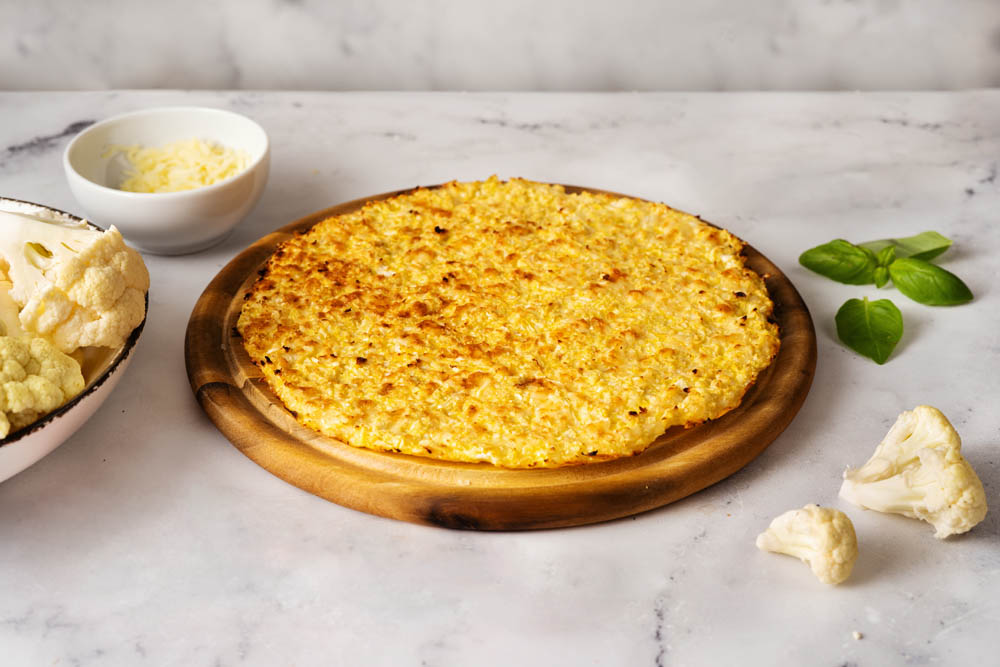 Healthy cauliflower pizza crust with ingrediets on white table. Keto diet and low carb food concept. Vegetarian food