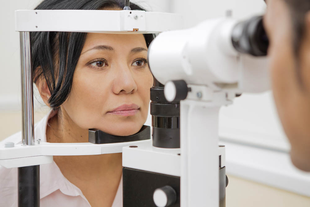 A woman undergoing an eye examination using a slit lamp at an optometrists office.
