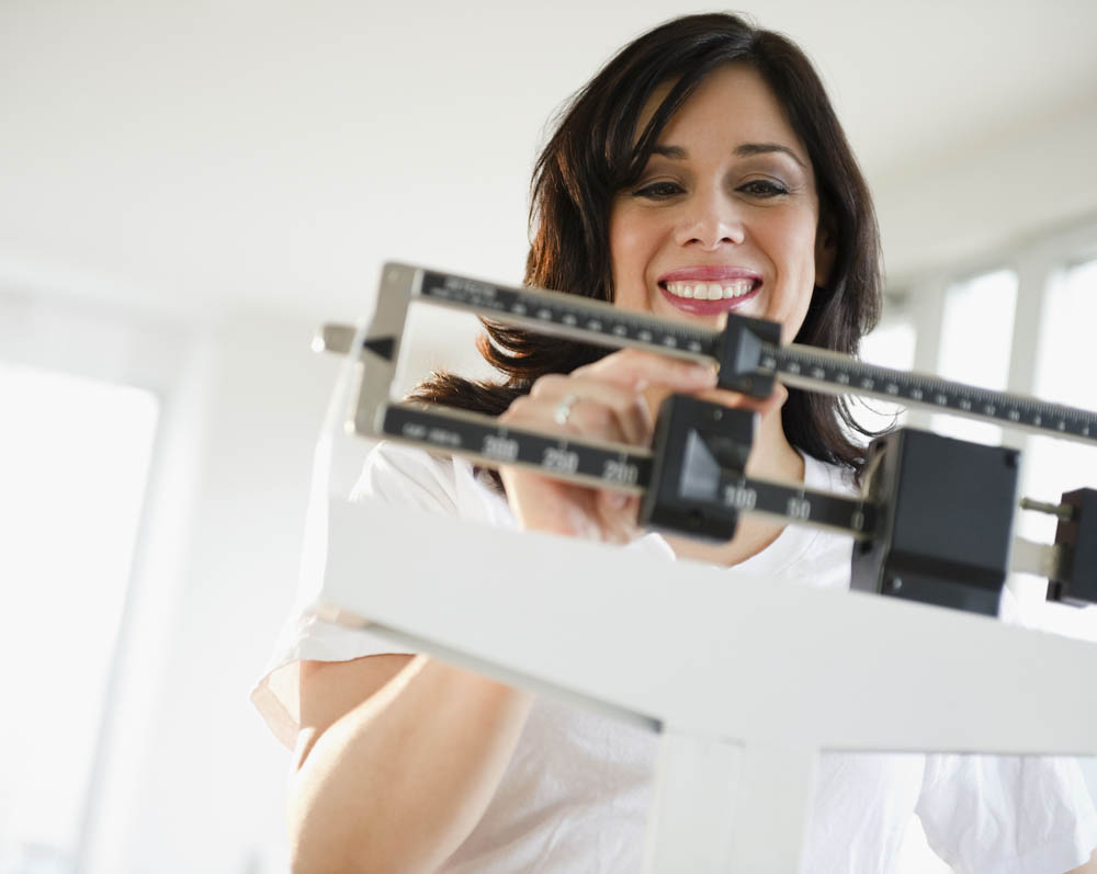 Person adjusting a balance scale, smiling and wearing a white shirt in a bright room.