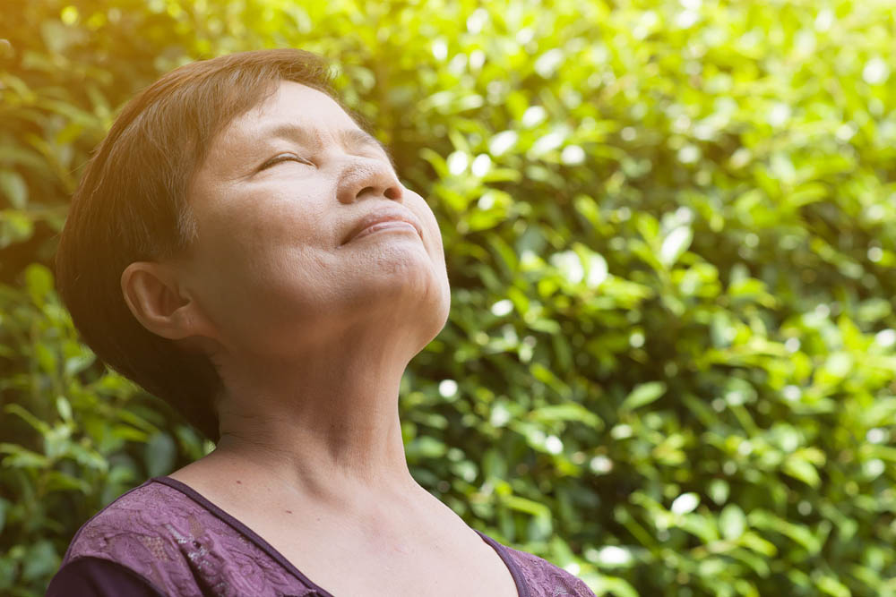 Woman outdoors with eyes closed, taking a deep breath and enjoying the sunlight