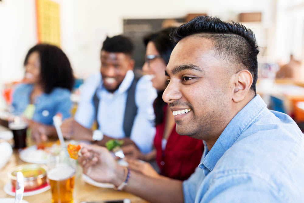 leisure, food and people concept - group of happy international friends eating and talking at restaurant table