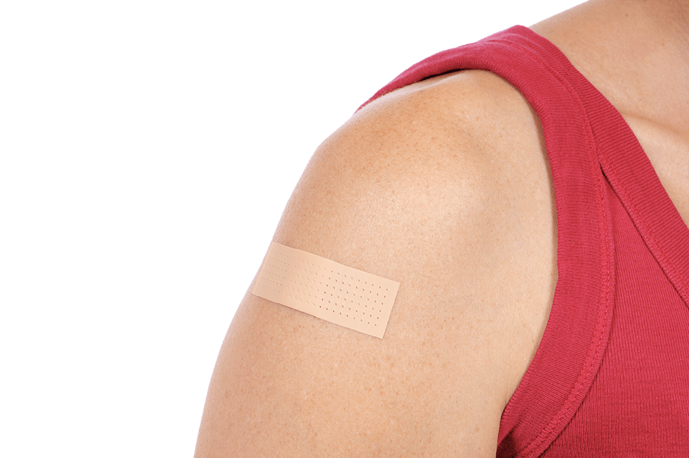 Person wearing a red tank top with a beige adhesive bandage on their upper arm, against a white background.