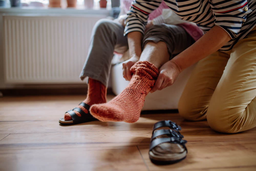 Unrecognizable senior woman getting help from caregiver with putting on socks.