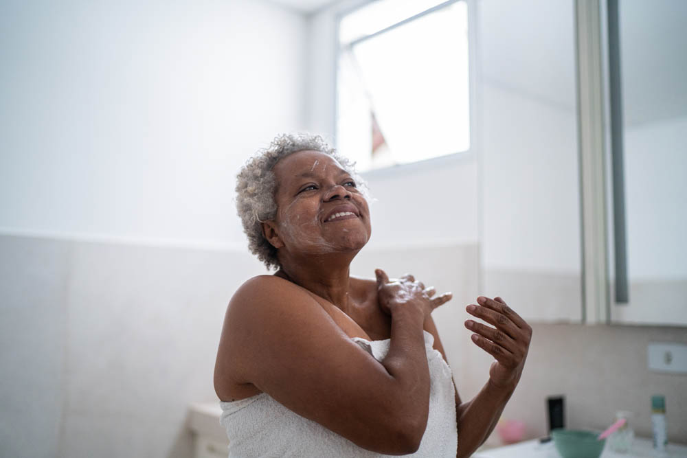 Senior woman applying body moisture in the bathroom at home