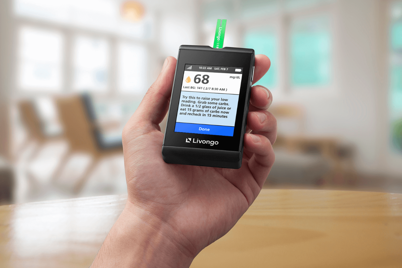 Hand holding a Livongo blood glucose meter displaying a reading of 68 mg/dL with a message providing guidance.