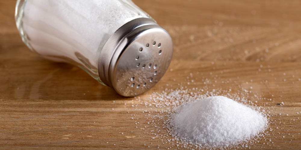 Salt shaker on its side with some salt in a pile on a wooden surface