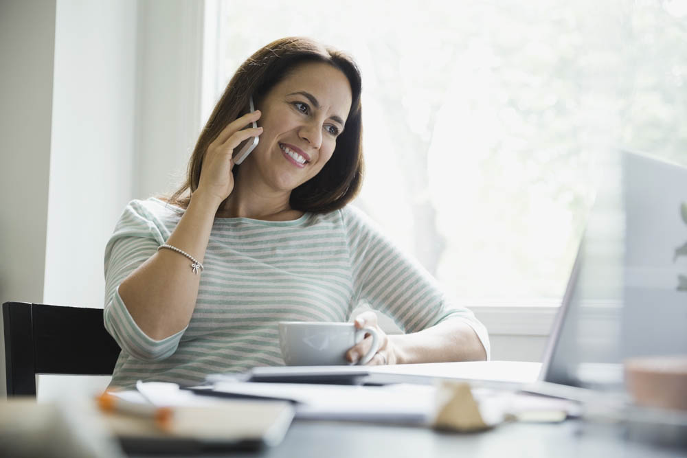 Smiling businesswoman using smart phone in home office