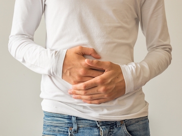 Person in a white long-sleeve shirt and jeans holding their stomach with both hands.