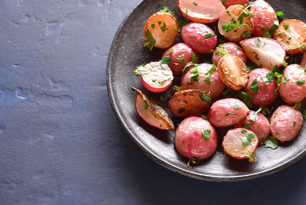 Roasted radish on plate over blue stone background with copy space. 